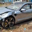 A mangled Porsche sports car and a damaged motorcycle lie at the scene of a nighttime accident, with police lights flashing in the background.