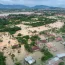 A flooded village in West Sumatra, by indonesia floods, with houses submerged in muddy water and debris scattered around. Mount Marapi can be seen in the background.